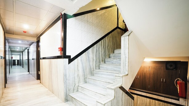 A marble staircase with black handrails leading to a wooden door with a fire extinguisher. - Hotel Kings Palace (Mumbai)