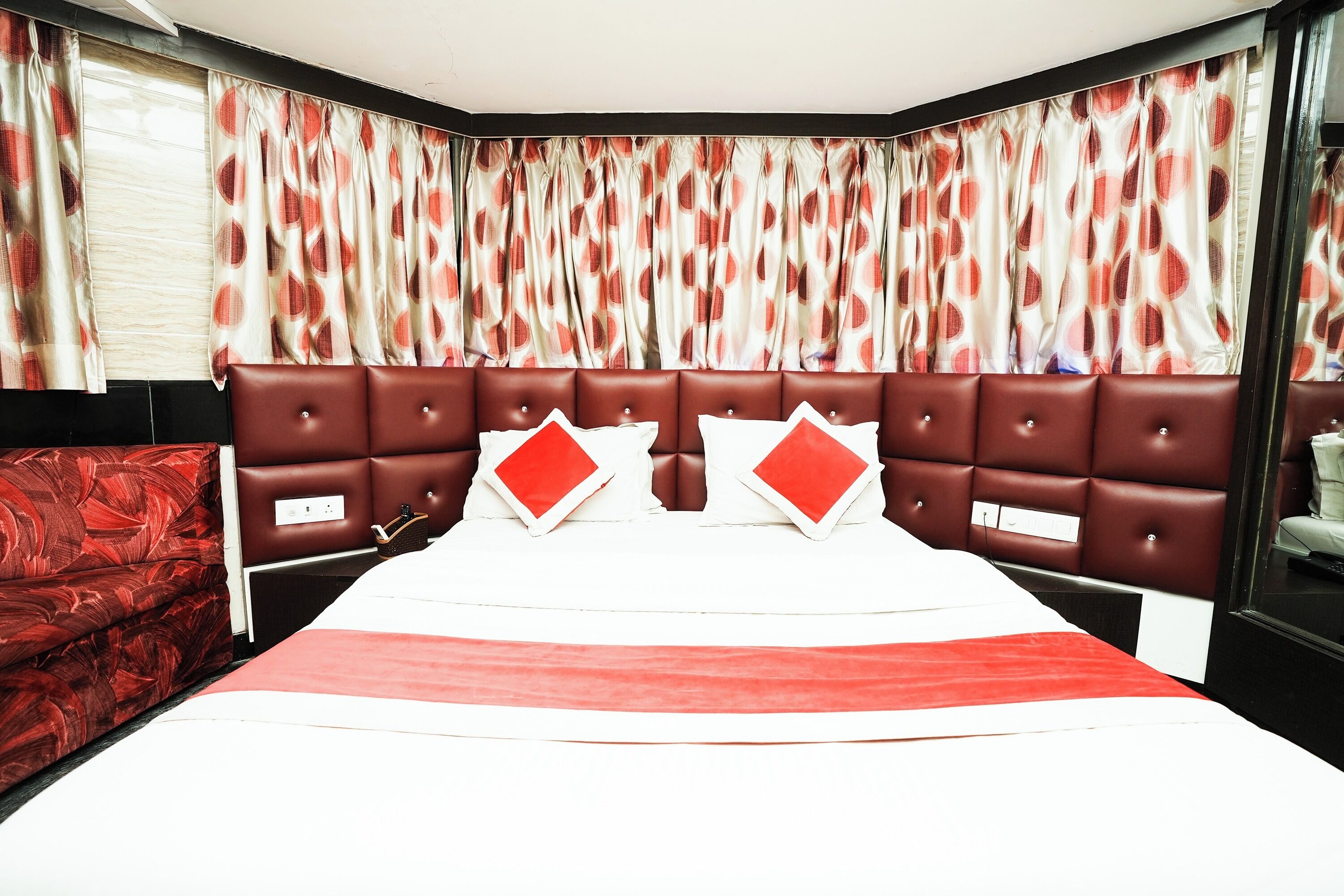 A hotel room with a large bed, red and white curtains, and a red upholstered headboard.