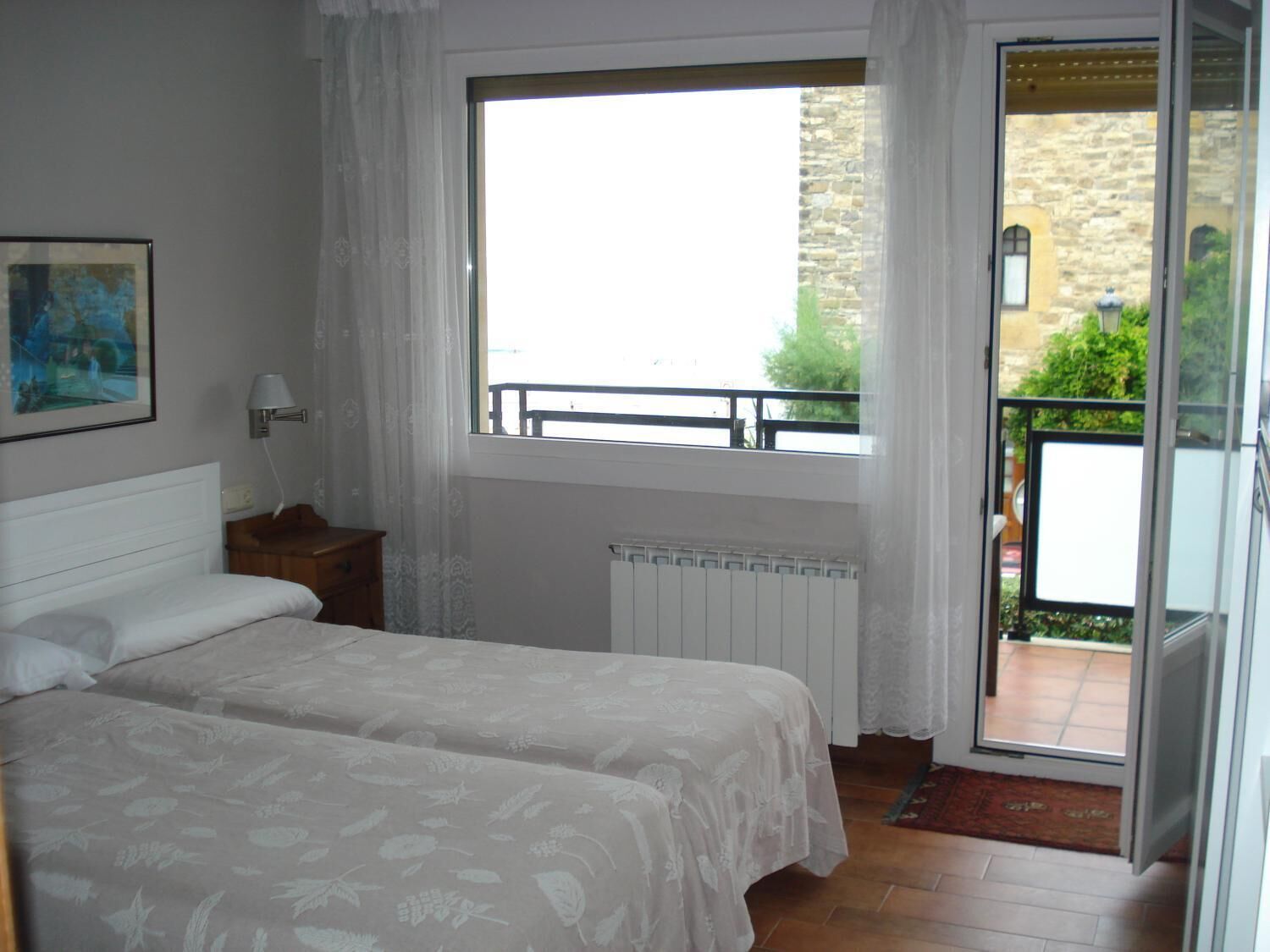 Un dormitorio con dos camas, una ventana, un radiador y vistas al balcón exterior.