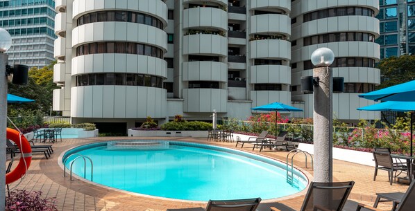 Una piscina rodeada de sillas de descanso y sombrillas, con un edificio moderno al fondo.