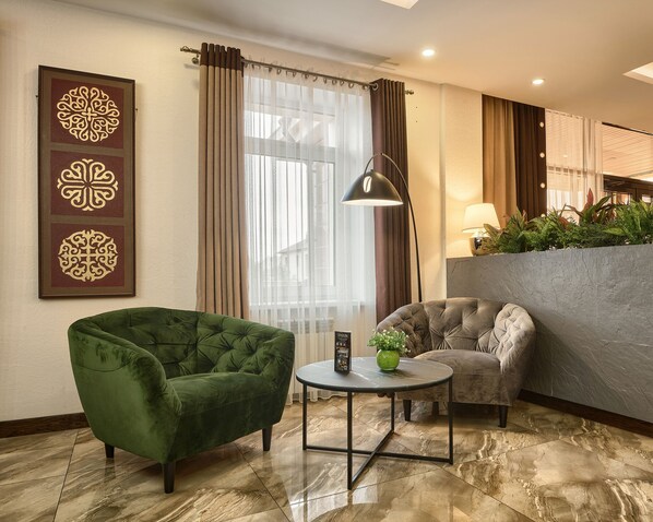 A hotel room with a green armchair, a grey armchair, a small round table with a vase, and a large window with curtains. - Aisha Bibi Hotel & Spa (Astana)