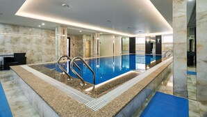 A modern indoor swimming pool with clear water, surrounded by marble walls and a blue floor mat. - Aisha Bibi Hotel & Spa (Astana)
