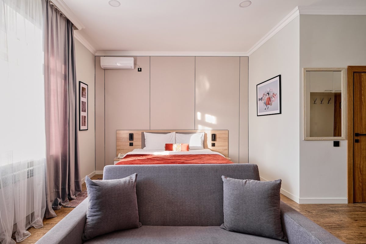 Une chambre à coucher moderne avec un lit, un canapé gris et une grande fenêtre avec des rideaux.