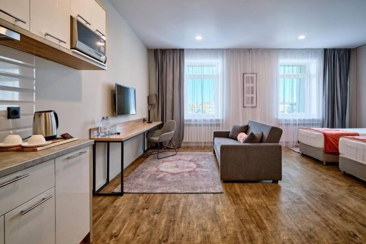 Une chambre d’hôtel moderne équipée d’une kitchenette, d’un canapé, d’une télévision et d’une grande fenêtre.