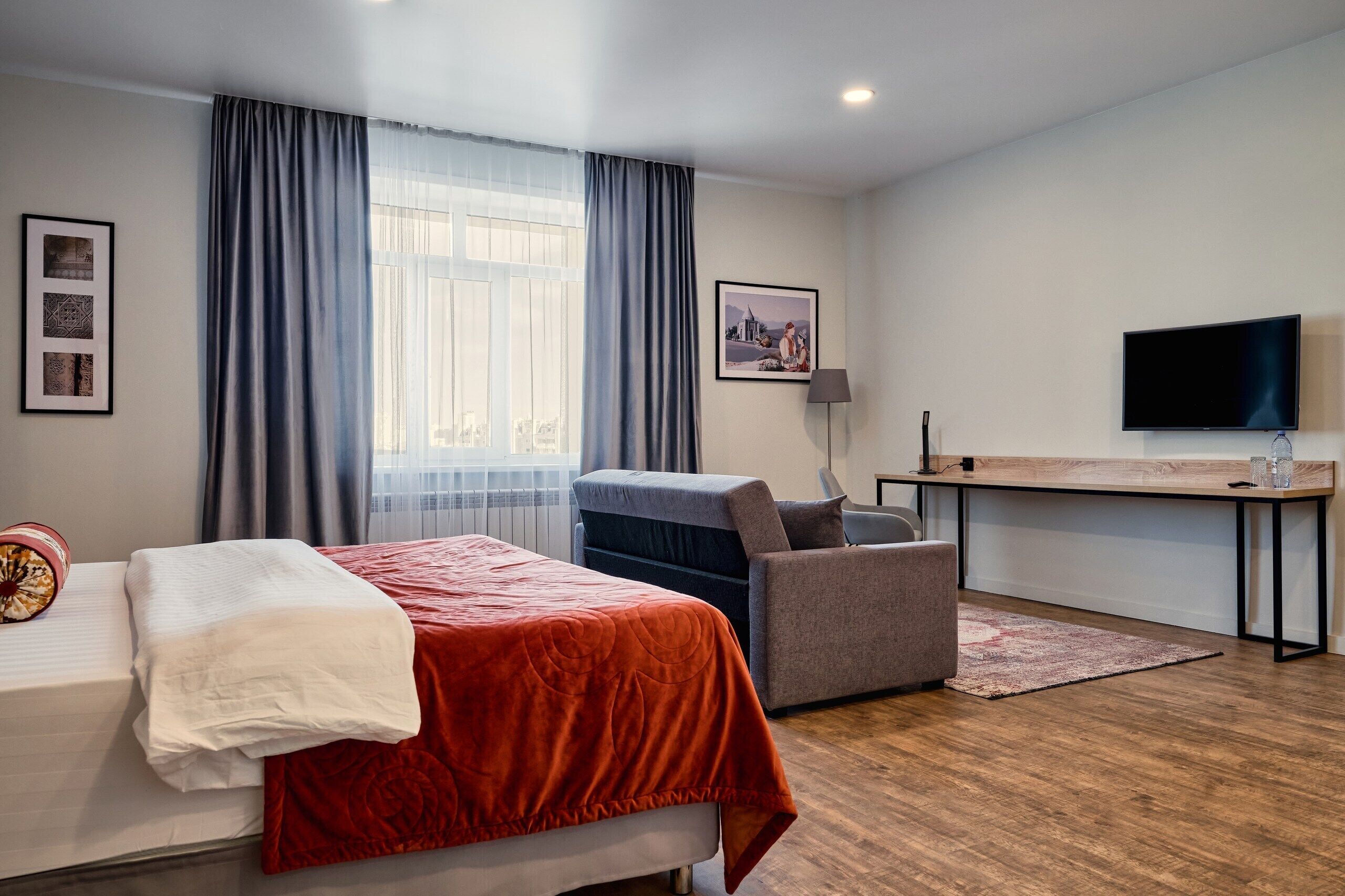 A hotel room with a bed, a desk, a chair, a TV, and a window with curtains.