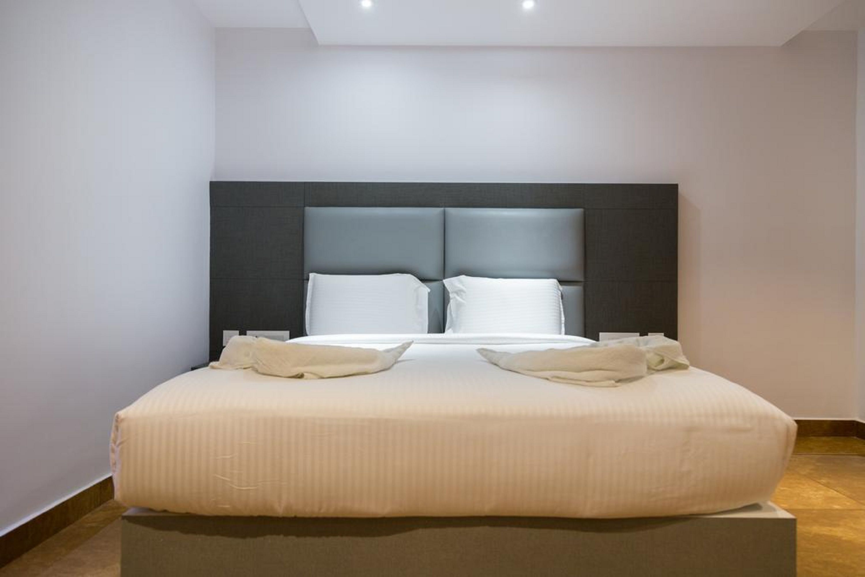 A modern hotel room with a large bed, a dark headboard, and a neutral color scheme.