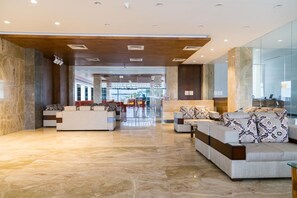 A spacious lobby with a marble floor, modern sofas, and a glass wall. - Hotel Hills (Tirupattur)