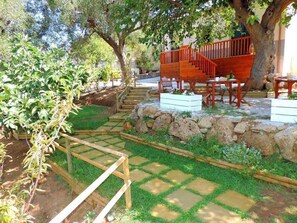 Un jardín con una escalera de madera, pared de piedra y una zona de estar con mesas y sillas.