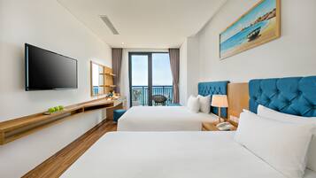 Habitación de hotel con dos camas, televisor, un cuadro y balcón con vistas.