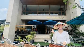 Una persona de pie frente al Hotel SeaShore, sosteniendo una bicicleta con cestas que dicen "SeaShore Hotel".