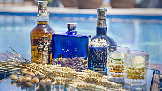 A poolside setting with three bottles of whisky and two glasses, surrounded by decorative elements. - Seashore Hotel & Apartment (Da Nang)