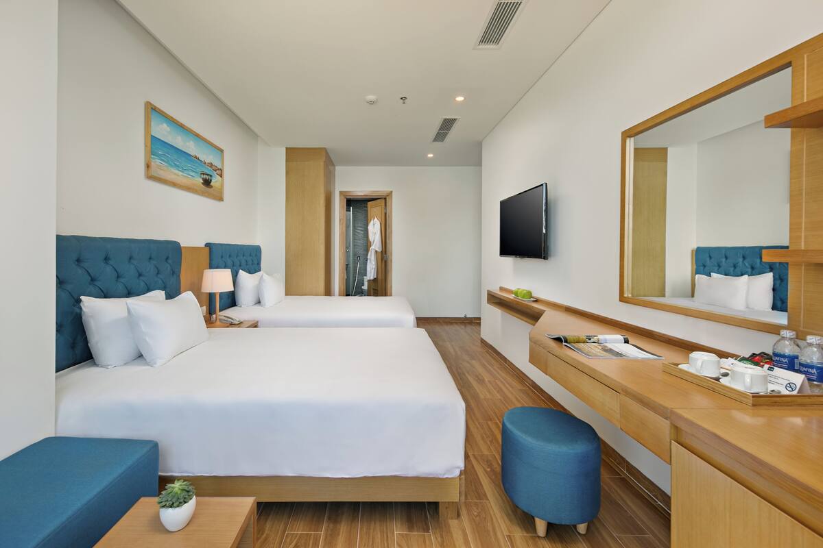 A hotel room with two beds, a desk, a mirror, a television, and a painting on the wall.