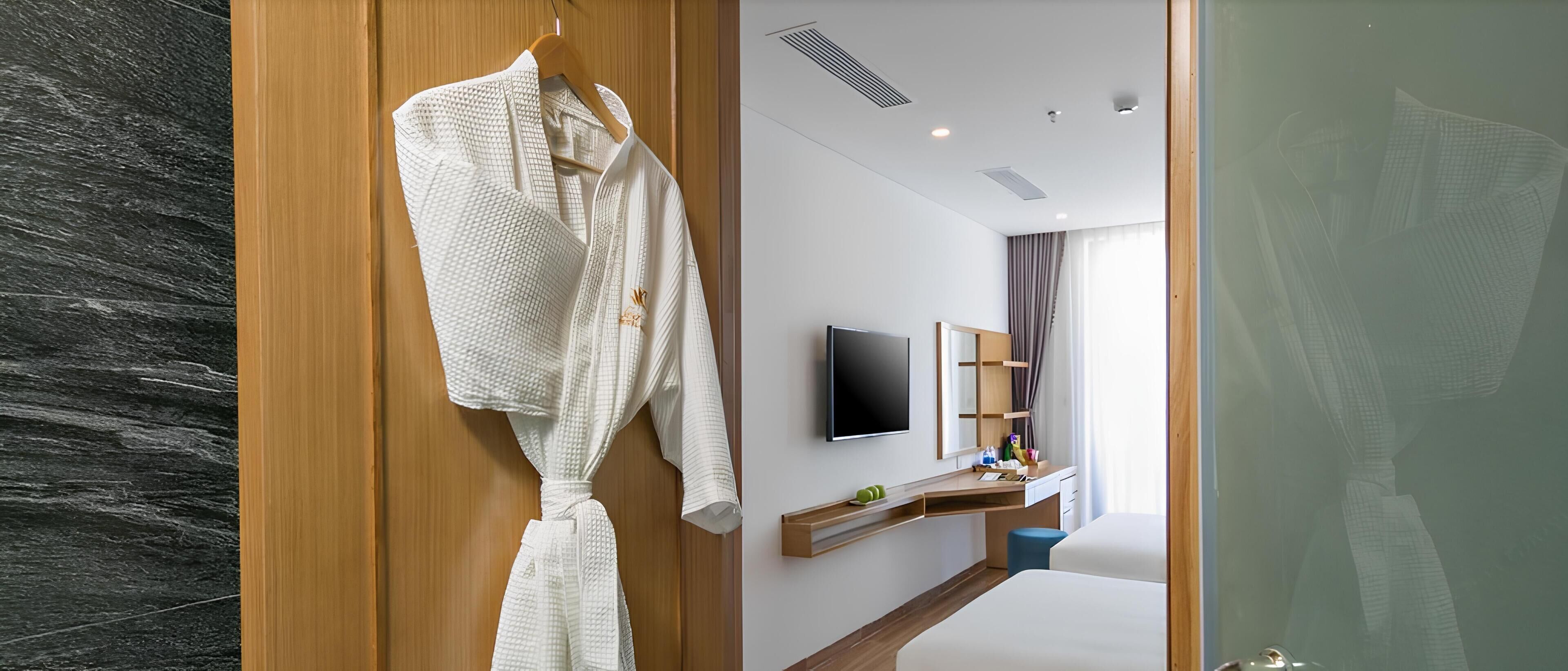 Un baño moderno con tocador de madera, televisor de pantalla plana y bata colgada en un perchero de madera.
