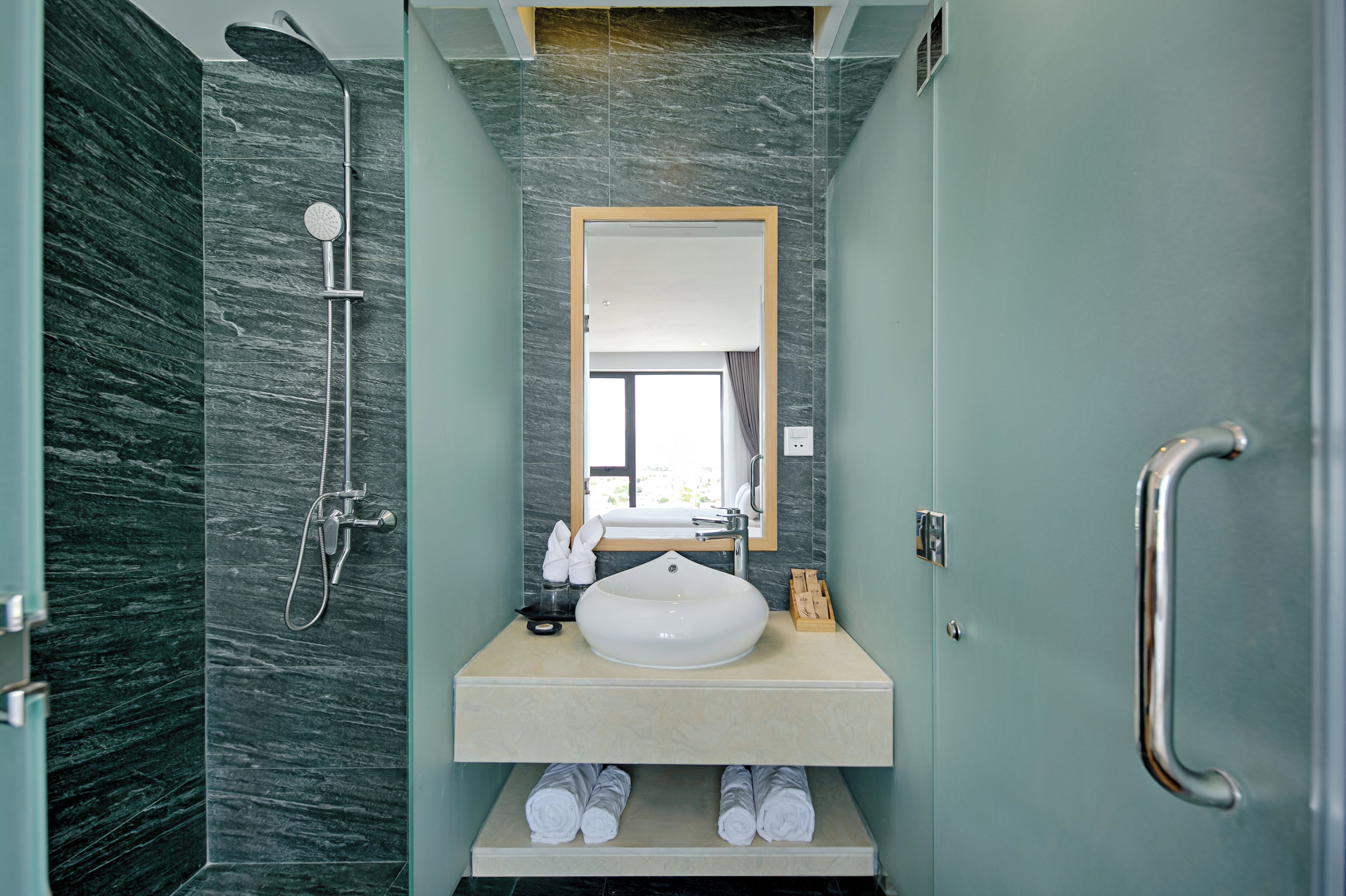 A bathroom with a marble shower, a sink with a mirror, and towels on the counter.