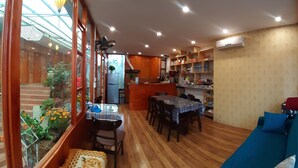 A cozy dining area with a wooden table and chairs, a kitchen in the background, and a view of a garden through a window. - Dang Khoa Garden Inn (Sa Pa)