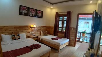 A hotel room with two beds, wooden headboard, wall-mounted lamps, a window with curtains, and a balcony with a hanging planter.
