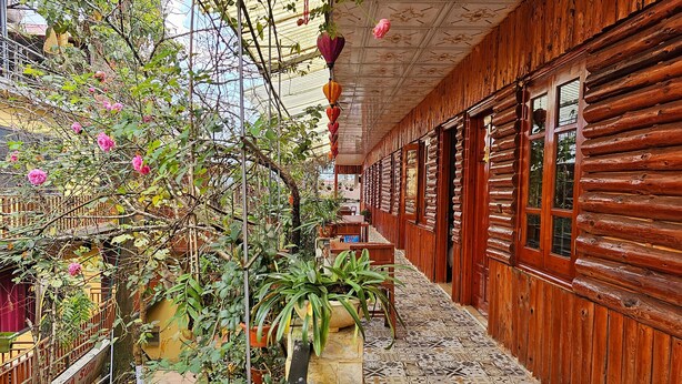 A wooden corridor with a tiled floor, potted plants, and a hanging flower. - Dang Khoa Garden Inn (Sa Pa)