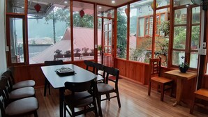 A dining area with a table and chairs, large windows with a view of buildings and greenery, and a wooden ceiling. - Dang Khoa Garden Inn (Sa Pa)