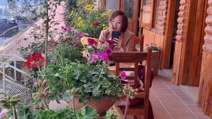A person seated at a table with potted plants and flowers, in a room with wooden walls and a tiled floor. - Dang Khoa Garden Inn (Sa Pa)
