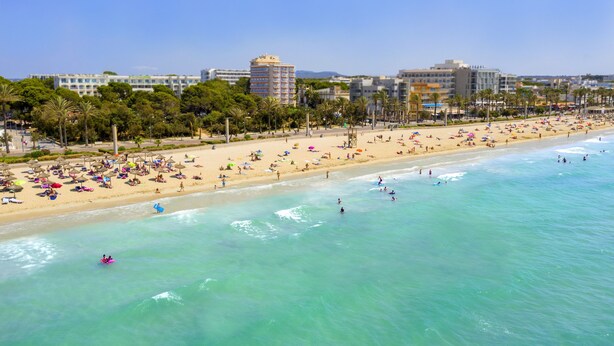 Ein Strand mit Menschen, die sonnenbaden, schwimmen und am Ufer entlangspazieren.