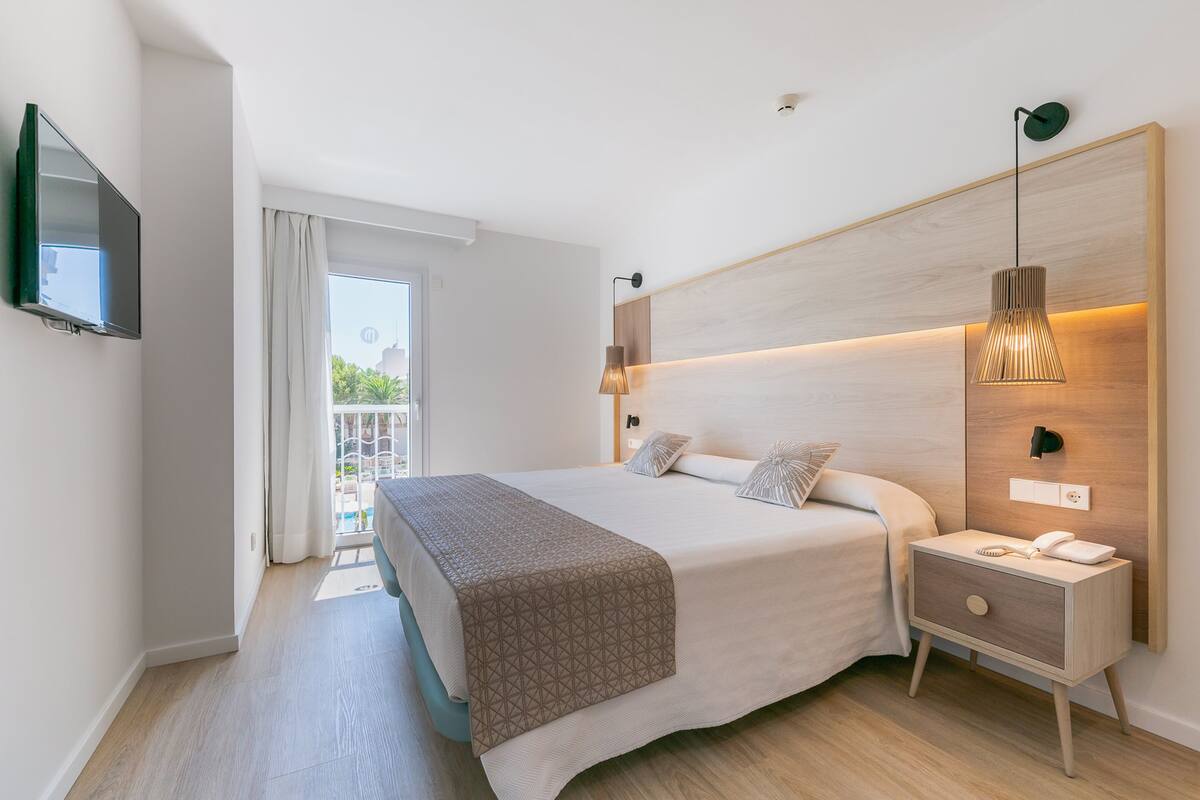 Une chambre d’hôtel moderne avec un grand lit, une table de chevet et un téléviseur fixé au mur.
