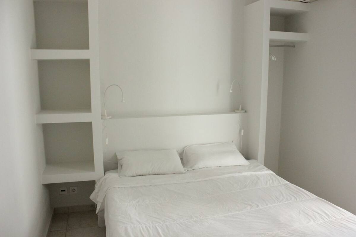 A bedroom with a bed, white walls, and built-in shelving.