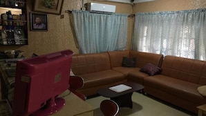 A living room with a brown leather sofa, a red TV, a coffee table, and a ceiling fan. - Hotel Princebella (Lagos)