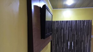 A room with a wooden panel wall, a mounted television, and a ceiling fan. - Hotel Princebella (Lagos)