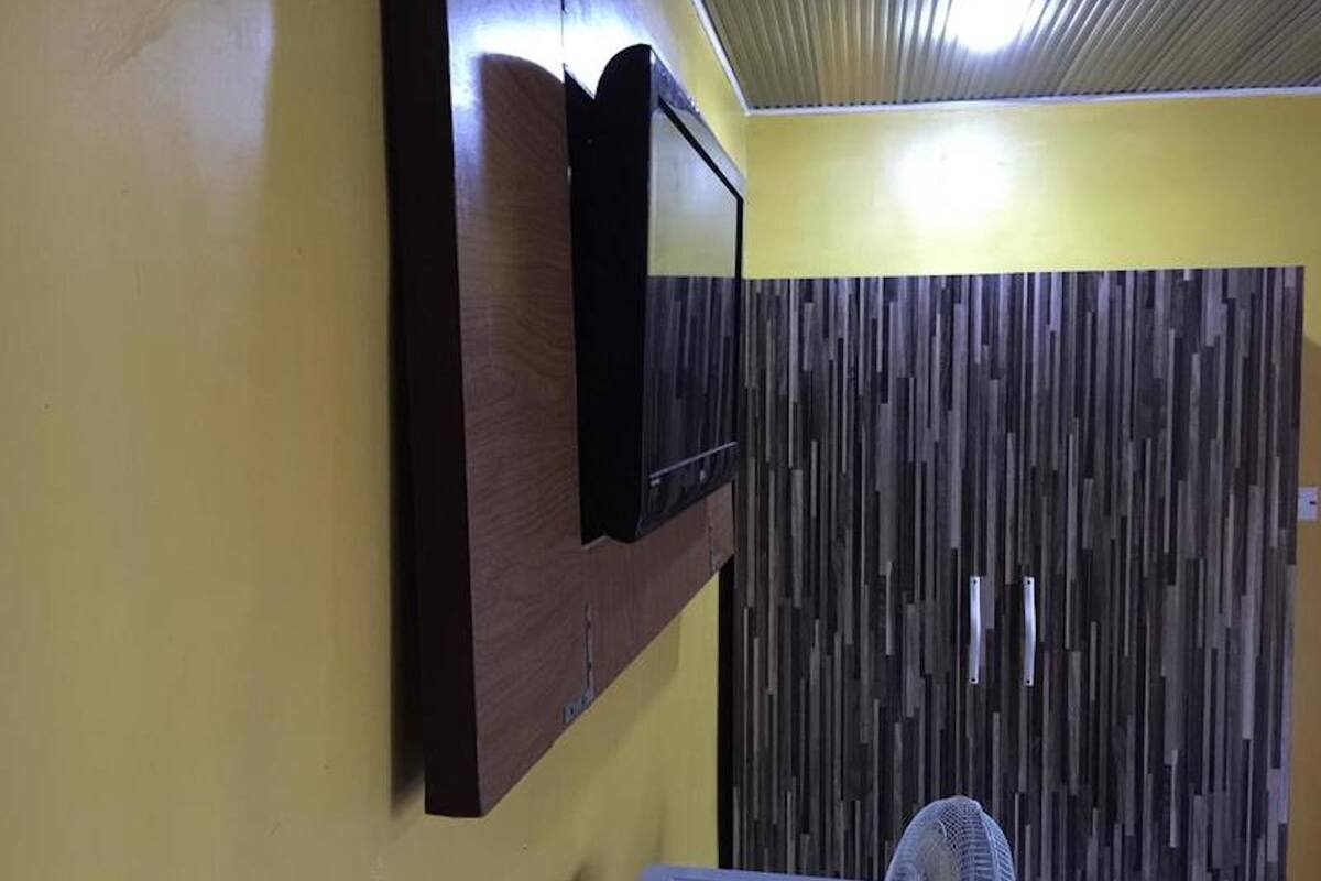 Una habitación con pared de paneles de madera, un televisor montado y un ventilador de techo.