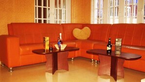A modern living room with a red leather sofa, two wooden side tables, and a heart-shaped cushion. - Hotel Princebella (Lagos)