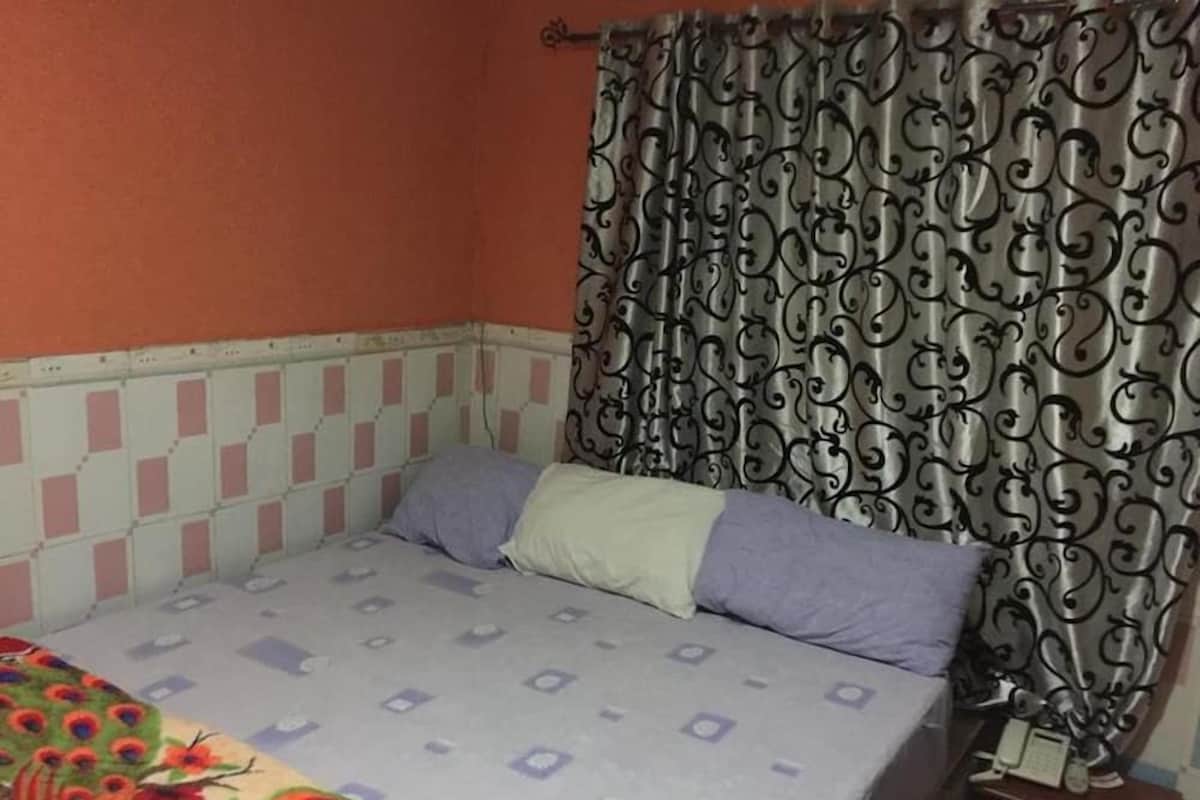 Un dormitorio con cama, almohadas, una mesita de noche y una cortina estampada.