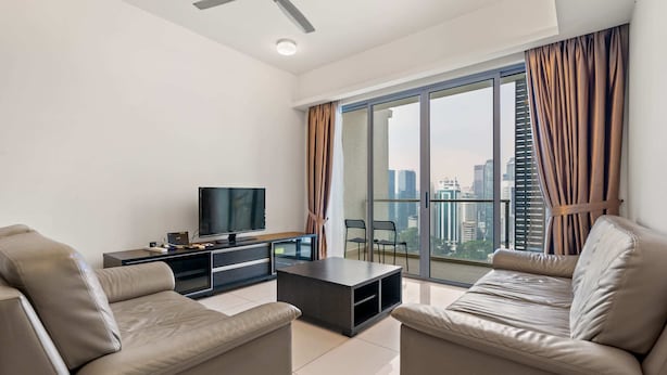 Un salon moderne doté d’un téléviseur à écran plat, de deux canapés en cuir, d’une table basse et d’une porte-fenêtre coulissante donnant sur un balcon avec vue sur la ville.