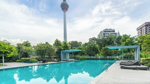 Une piscine dotée de chaises longues et d’un espace d’observation, entourée de verdure et avec une haute tour en arrière-plan.