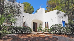 A white stucco building with a central archway, a blue door, and a small garden with cacti and shrubs. - Villa Marechiaro (Racale)