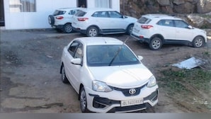 Une voiture Toyota blanche est garée devant un immeuble doté d’un balcon.