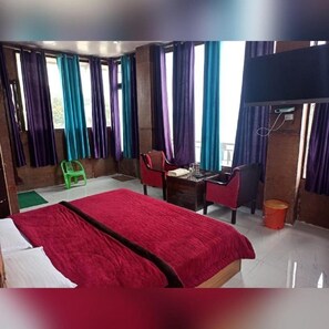 A hotel room with a bed, a desk, a chair, a television, and a window with curtains. - Silver Dew Resorts (Dehradun)