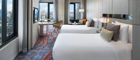 A hotel room with two beds, a desk, a chair, a TV, and a view of the city.