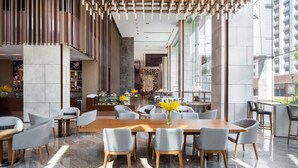 Uma sala de jantar moderna com uma mesa de madeira comprida e cadeiras estofadas cinzas, teto de madeira decorativo e grandes janelas com vista para a cidade.