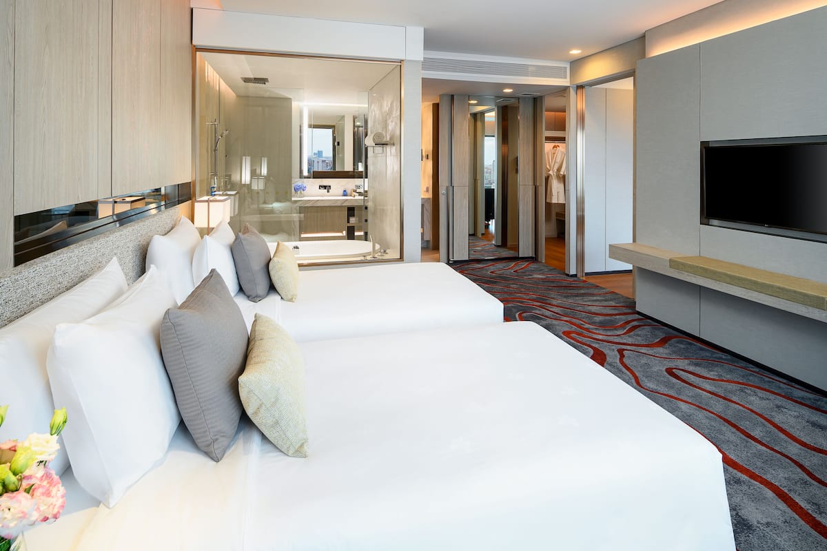 A hotel room with two beds, a TV, a bathroom with a mirror, and a view of the city.