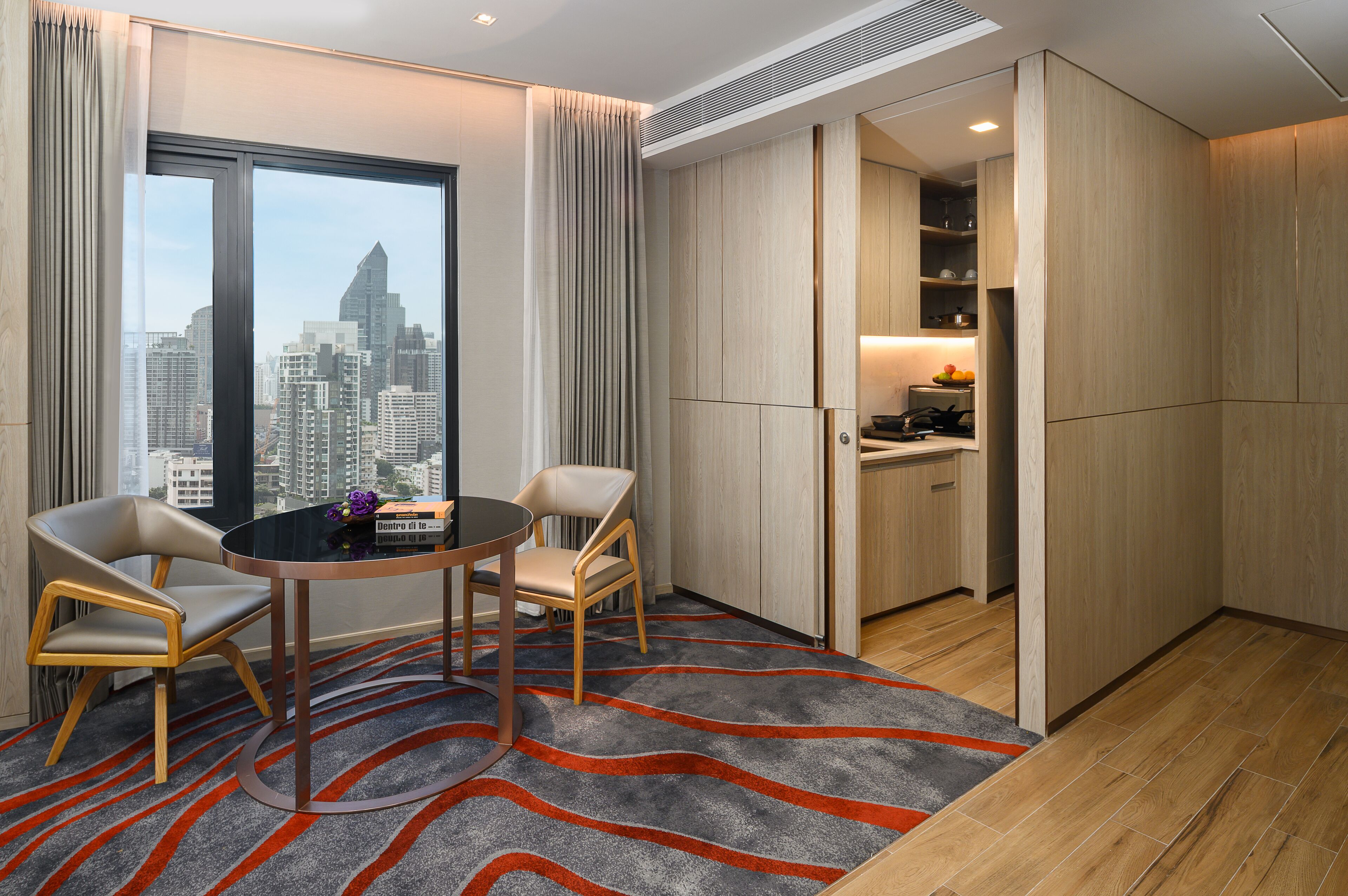 Ein modernes Hotelzimmer mit Stadtblick, einem Essbereich mit zwei Stühlen und einem Tisch sowie einer Küchenzeile.