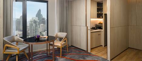 Ein modernes Hotelzimmer mit Stadtblick, einem Essbereich mit zwei Stühlen und einem Tisch sowie einer Küchenzeile.