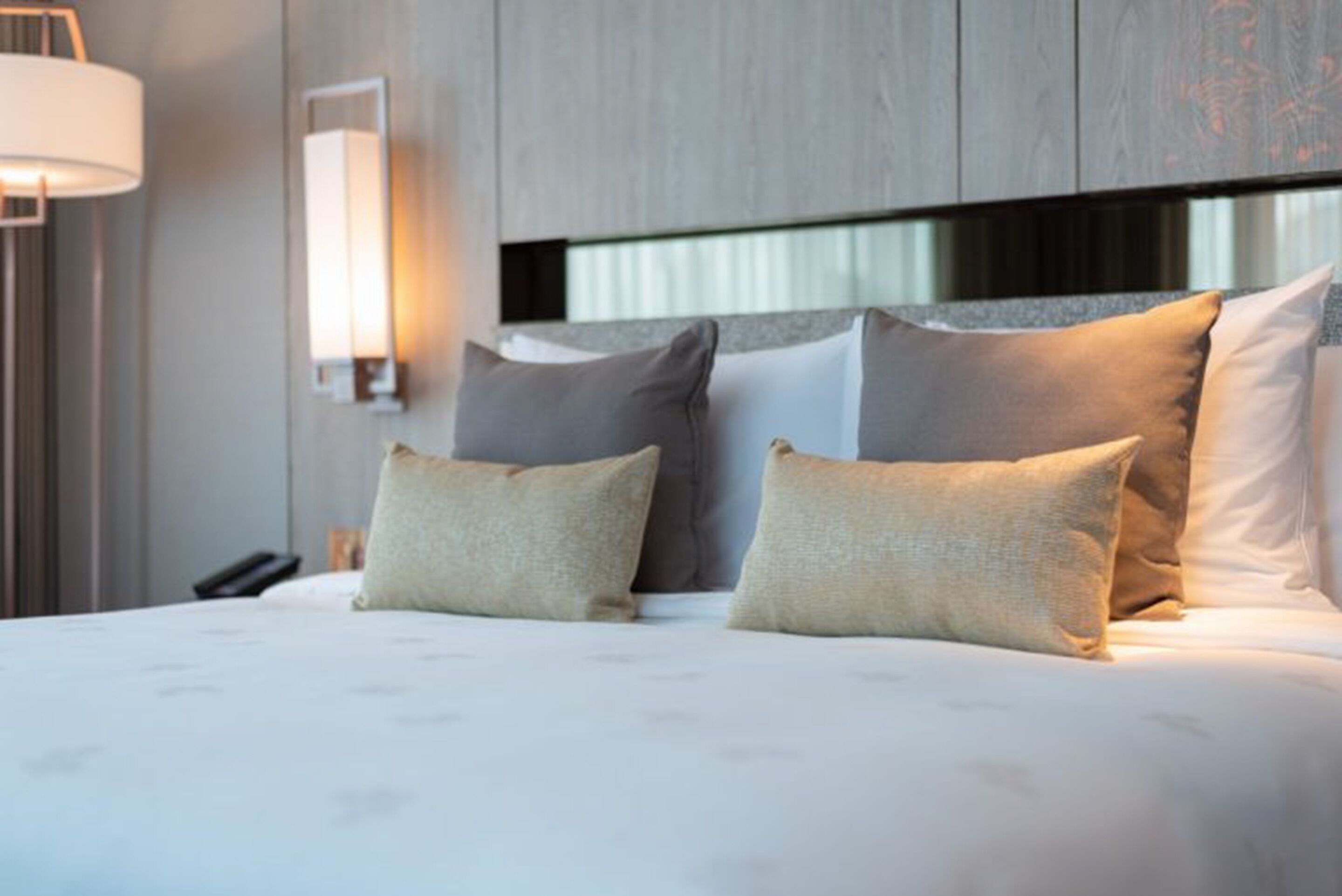 A hotel room with a large bed, multiple pillows, a bedside lamp, and a modern headboard.
