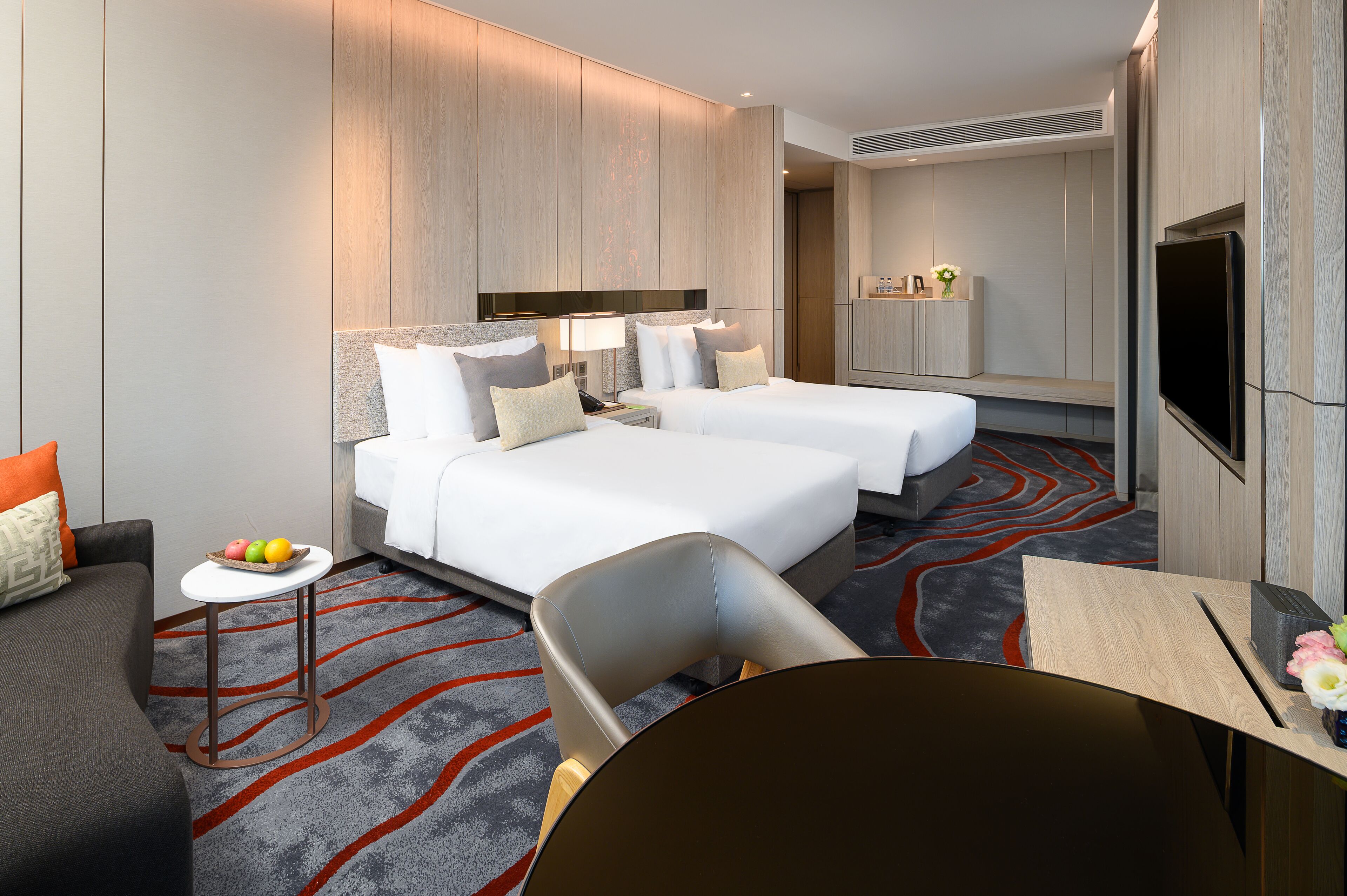 Une chambre d’hôtel avec deux lits, une petite table avec des fruits, une chaise, un canapé et un téléviseur.