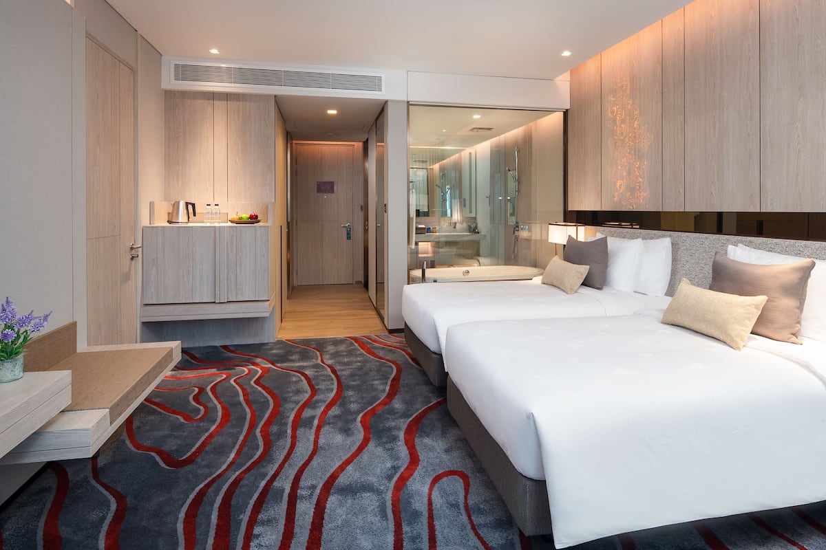 A modern hotel room with a large bed, a bedside table, a built-in wardrobe, a shower area, and a small kitchenette.