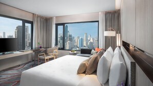 Quarto de hotel com uma cama grande, uma escrivaninha, uma cadeira, televisão e vista para a cidade.