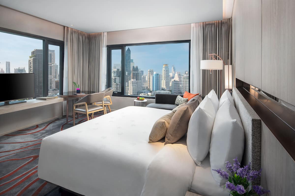 A hotel room with a large bed, a desk, a chair, a TV, and a city view.