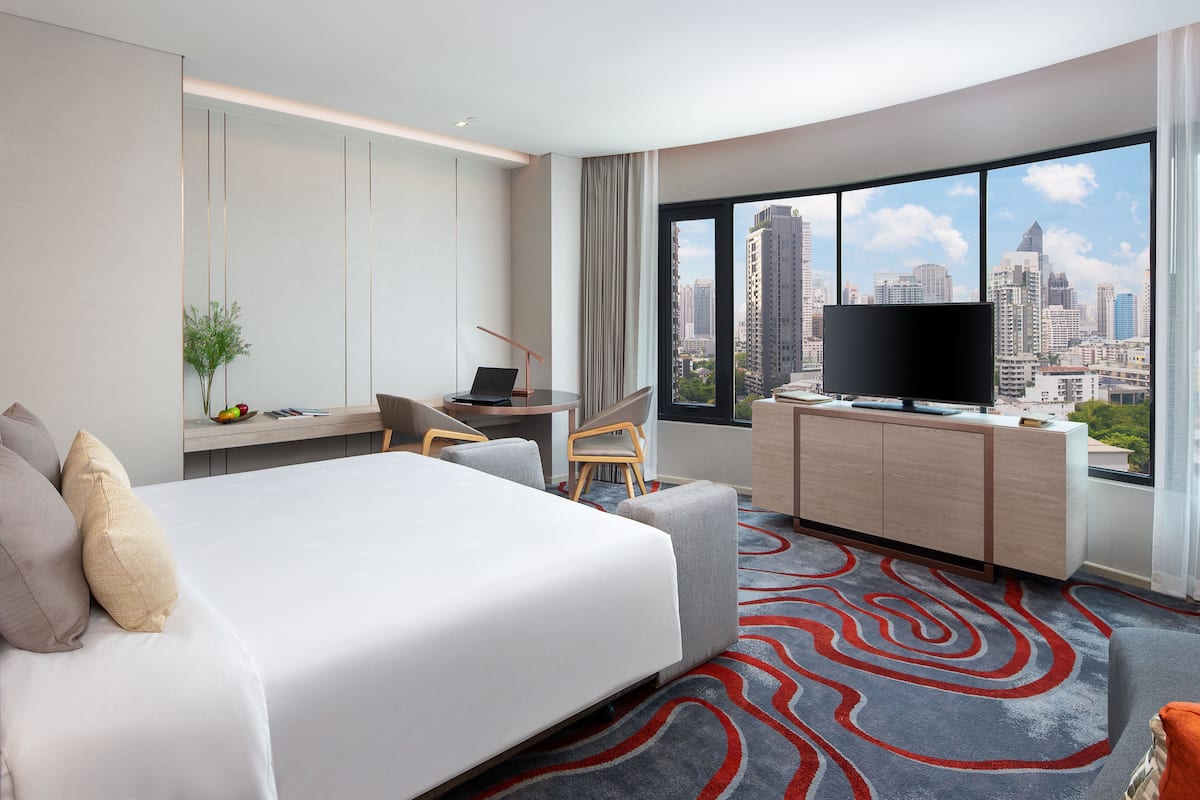 A hotel room with a bed, a desk, a TV, and a large window with a city view.