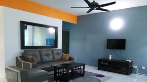 A modern living room with a grey sofa, a coffee table, a TV, and a ceiling fan. - Anjung Apartment 3BR 1 (Banting)
