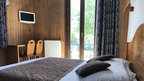 A wooden-paneled room with a bed, a small table with chairs, a radiator, and a window with curtains. - Hôtel des Lacs (Chamonix-Mont-Blanc)