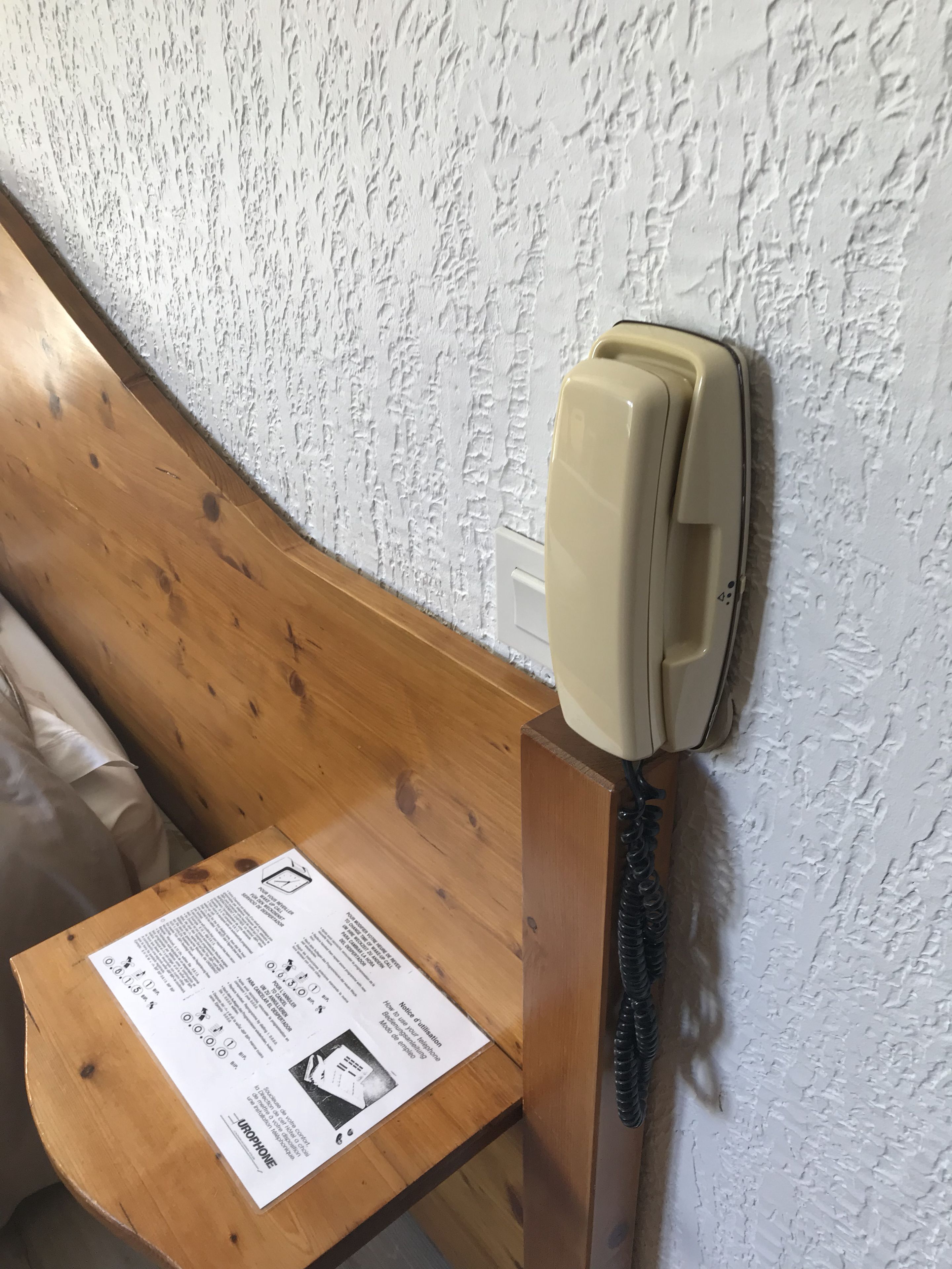 Un teléfono sujeto a una pared de madera con un manual de instrucciones impreso sobre una mesa de madera.